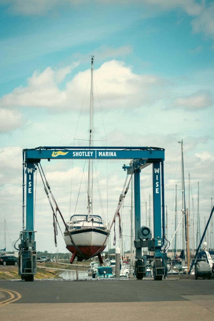 A sailboat is lifted by a crane at Shotley Marina, England, on a sunny day.